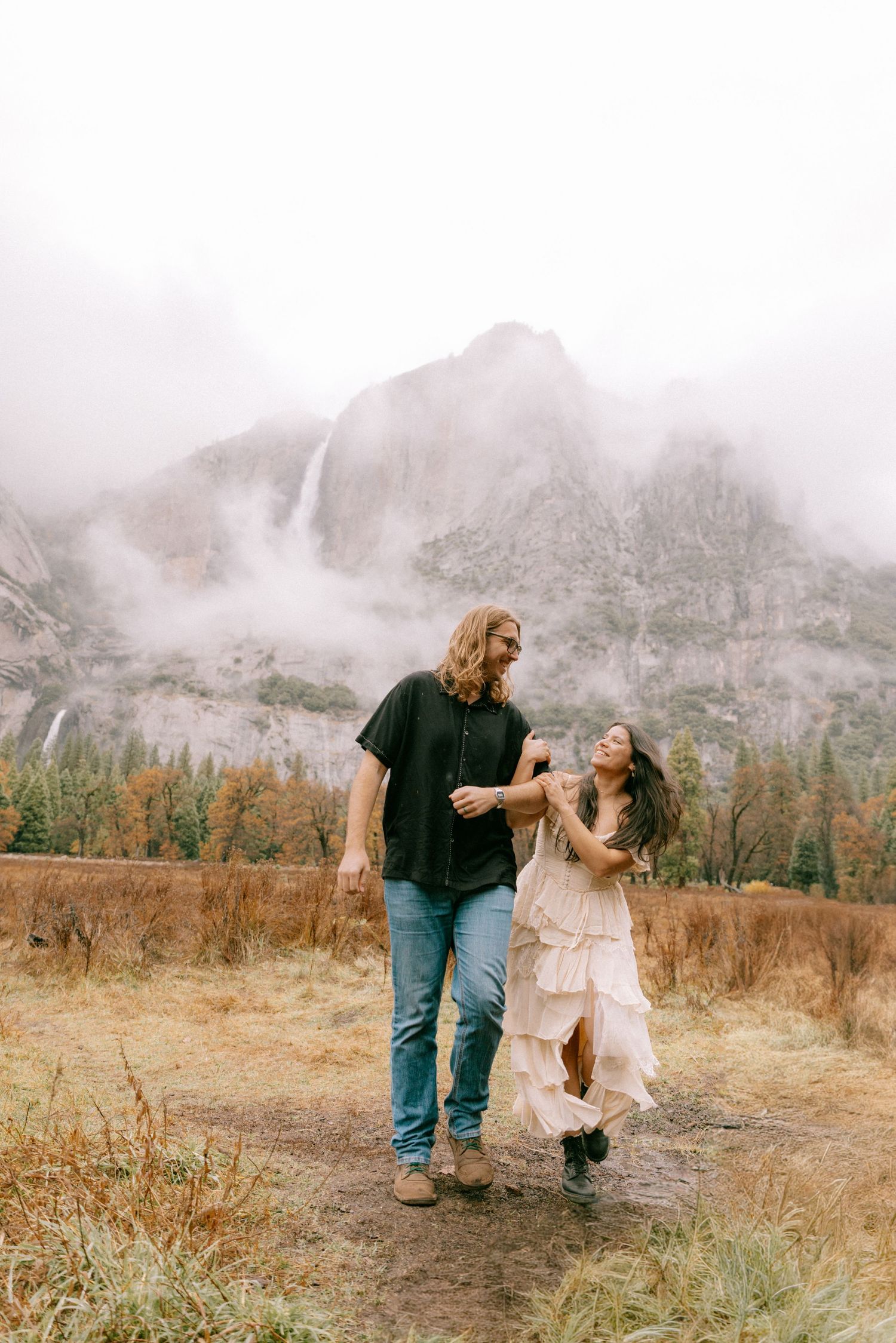 A couple shares tender moments in a misty mountain meadow with dramatic fog-covered peaks in the background.