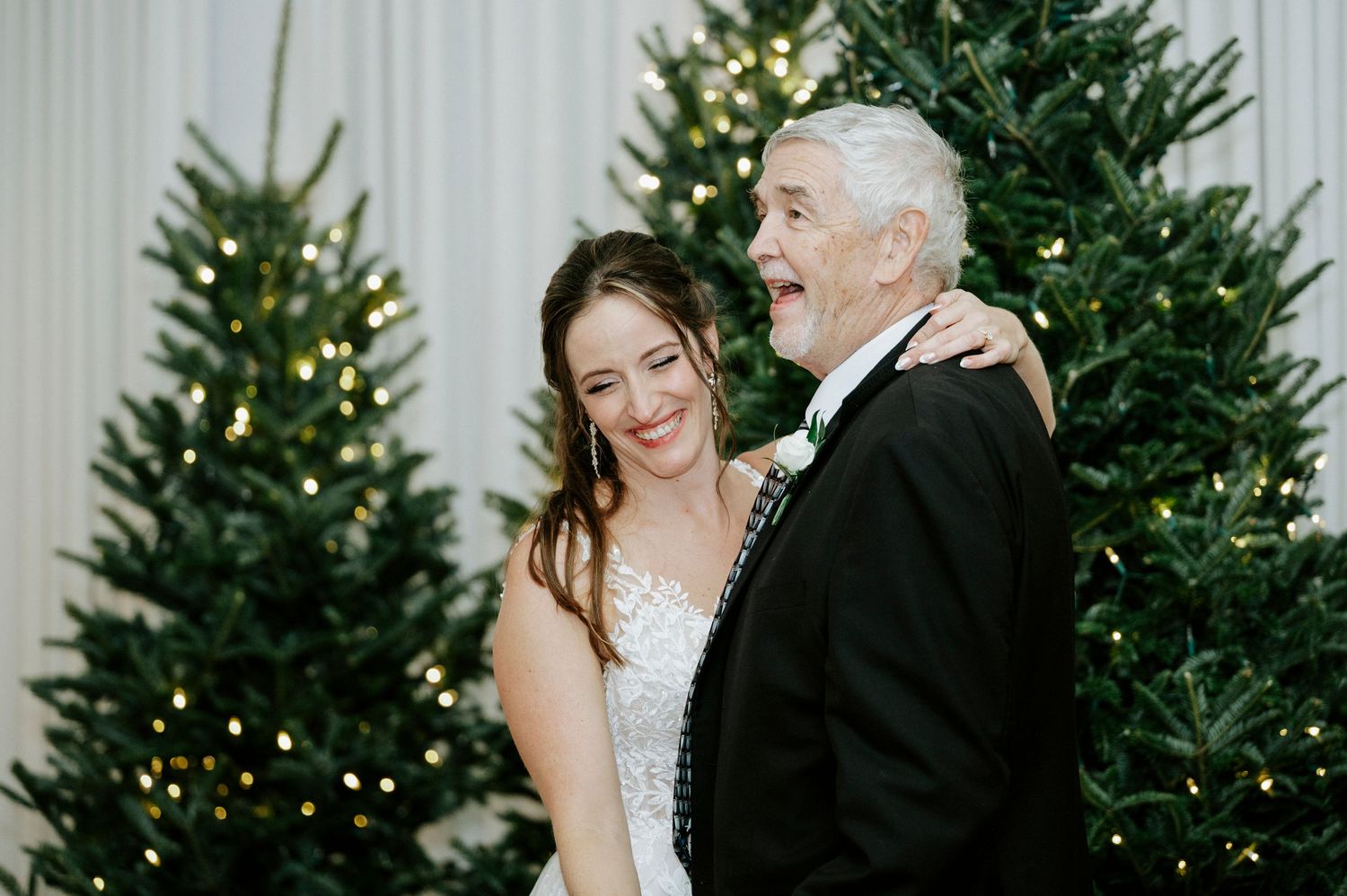 Bride and groom share a joyful moment together surrounded by Christmas trees during their winter wedding celebration.