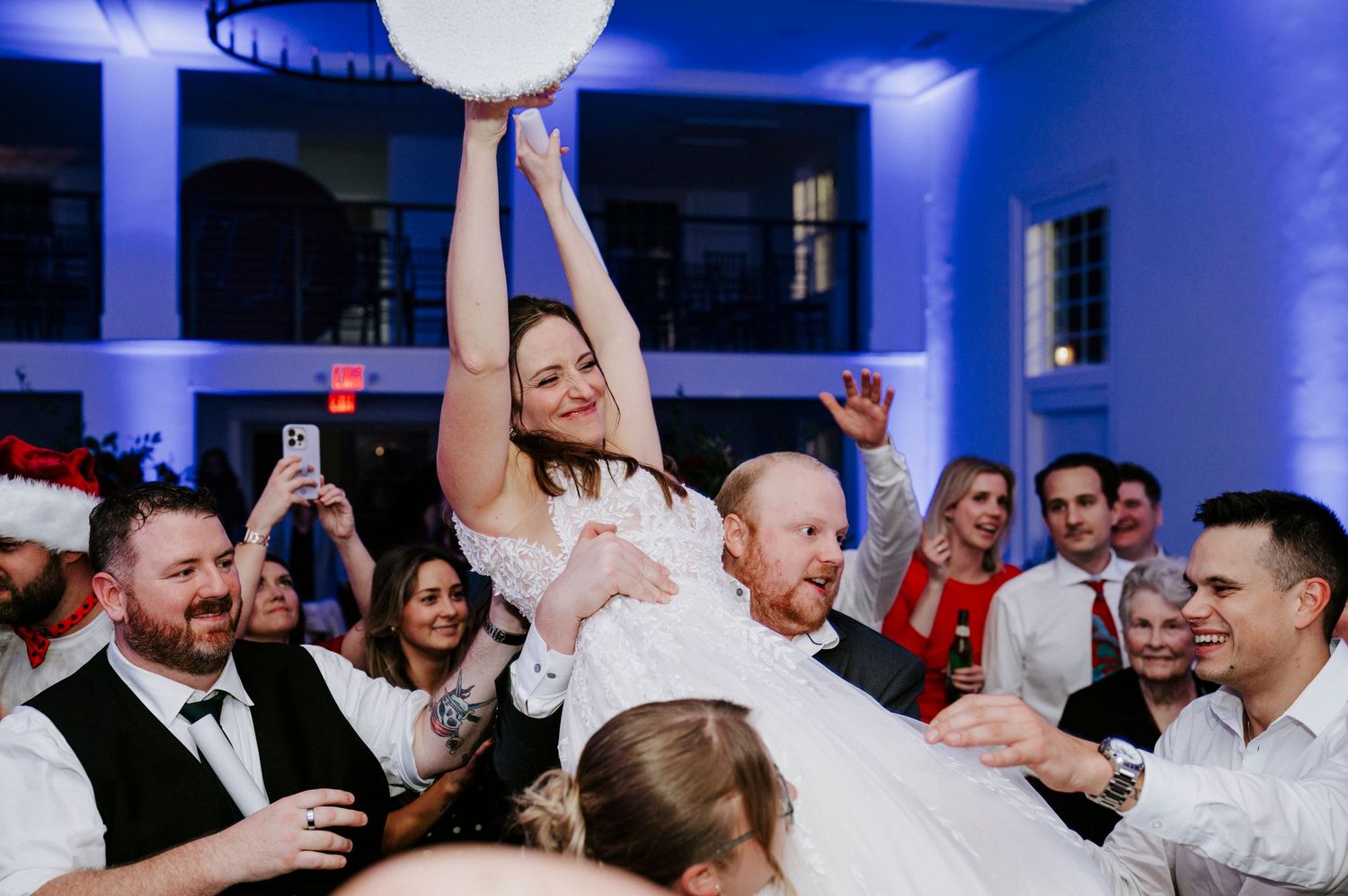 Wedding guests dancing and celebrating on a dance floor illuminated by blue lighting at a reception party.