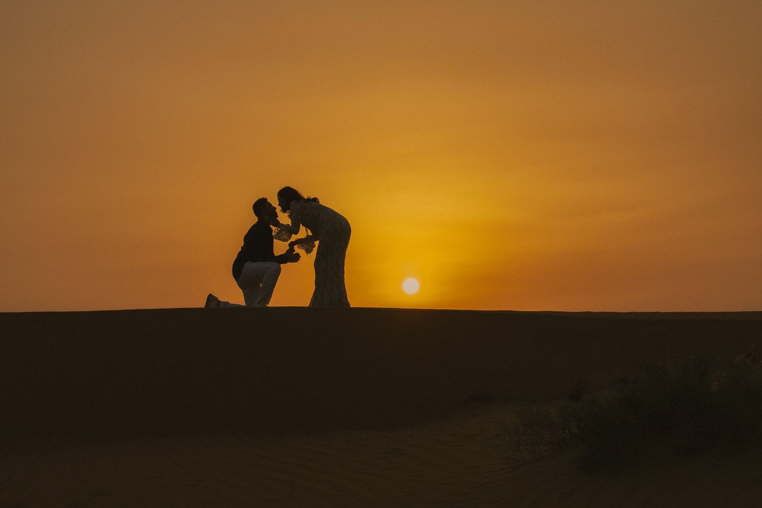 Surprise proposal photoshoot in Dubai desert – man kneeling to propose at sunset, silhouette