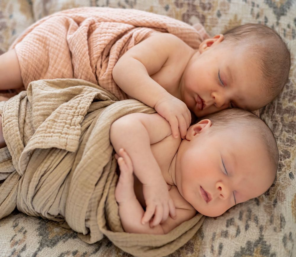 Sleeping newborn baby wrapped in soft beige fabric lying on textured neutral backdrop.