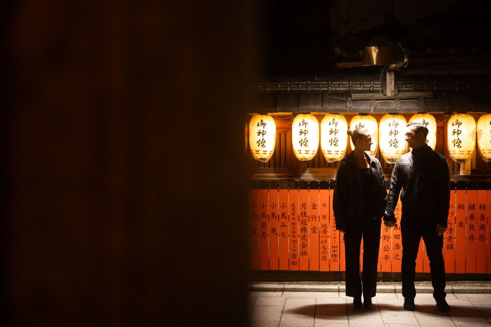 Couple holding hands silhouetted against glowing Japanese paper lanterns at a traditional shrine.