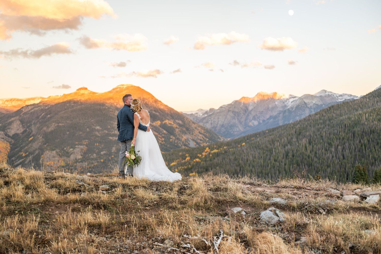 A bride and groom stand together on a mountain ridge with the snow-capped peaks of the San Juan mountains in the distance in the fall.