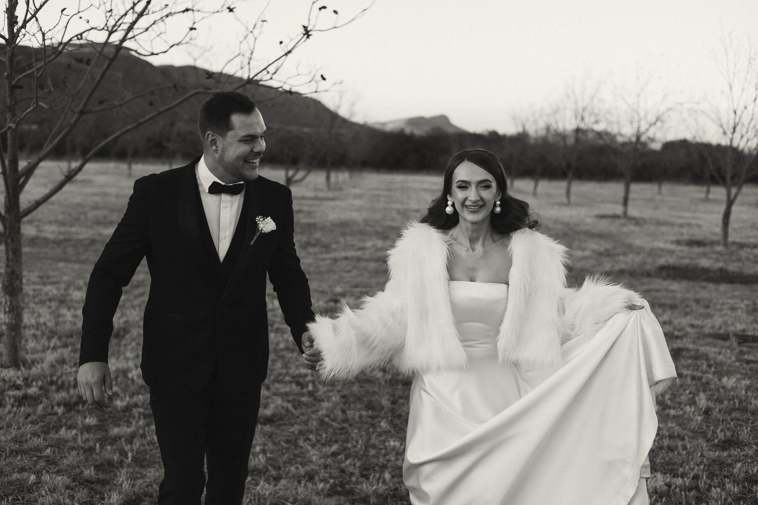 Couple walking through orchard field in formal wedding attire.