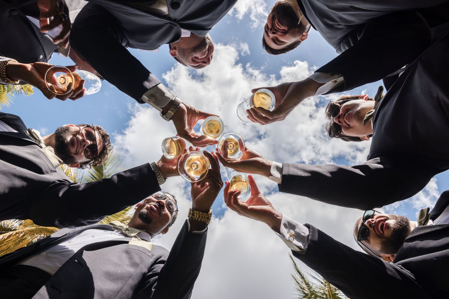 Business team members huddle together in a circle formation viewed from below against a bright blue sky.