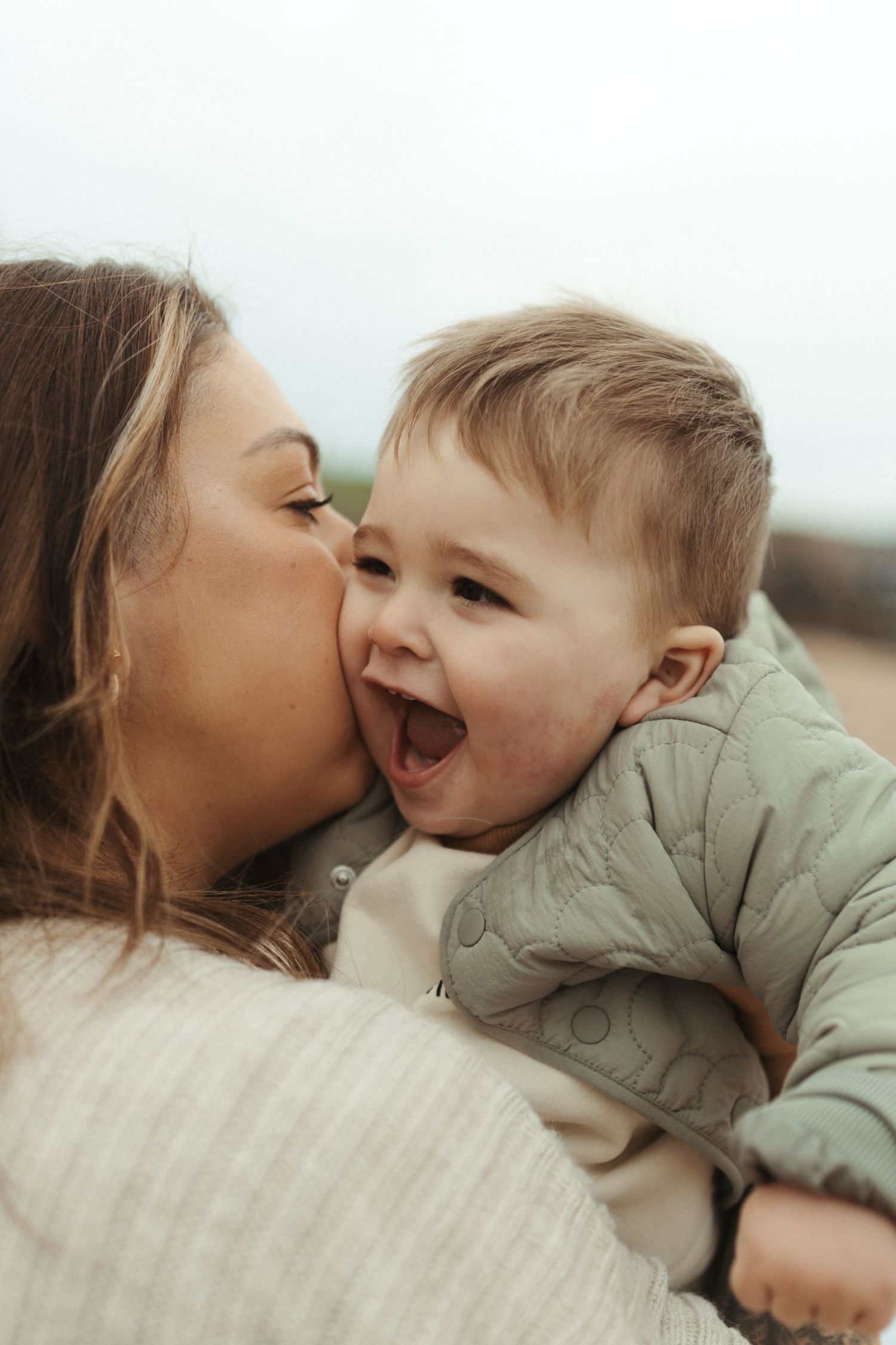 A joyful moment captured between parent and child sharing kisses and laughter in soft lighting.