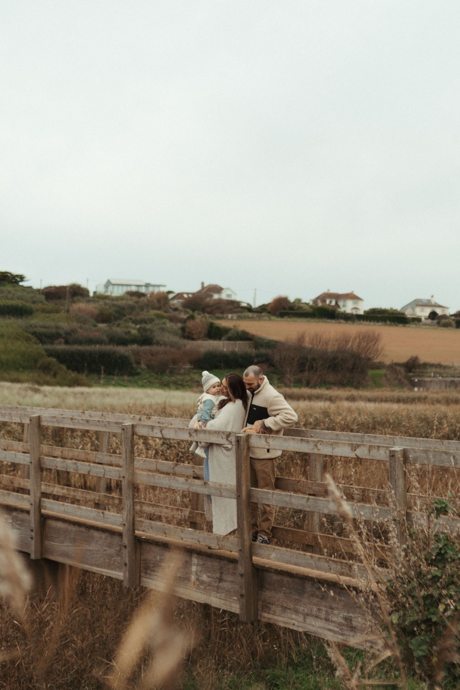 Wooden boardwalk railing stretches along a coastal path with houses visible in the distance.