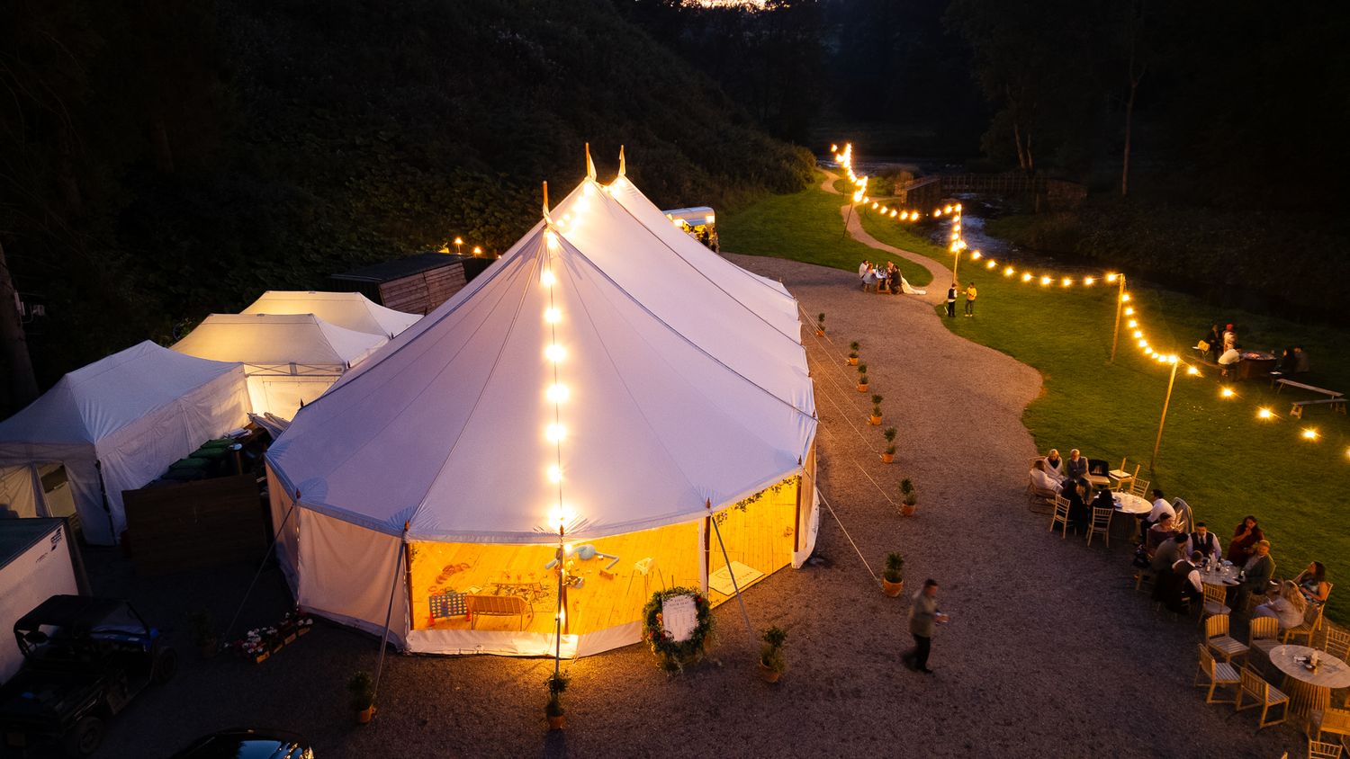 String lights illuminate a row of white glamping tents at night creating a magical outdoor camping atmosphere.