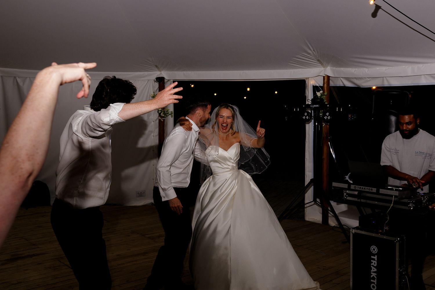 A bride and groom share their first dance at a wedding reception under a white tent with guests watching.