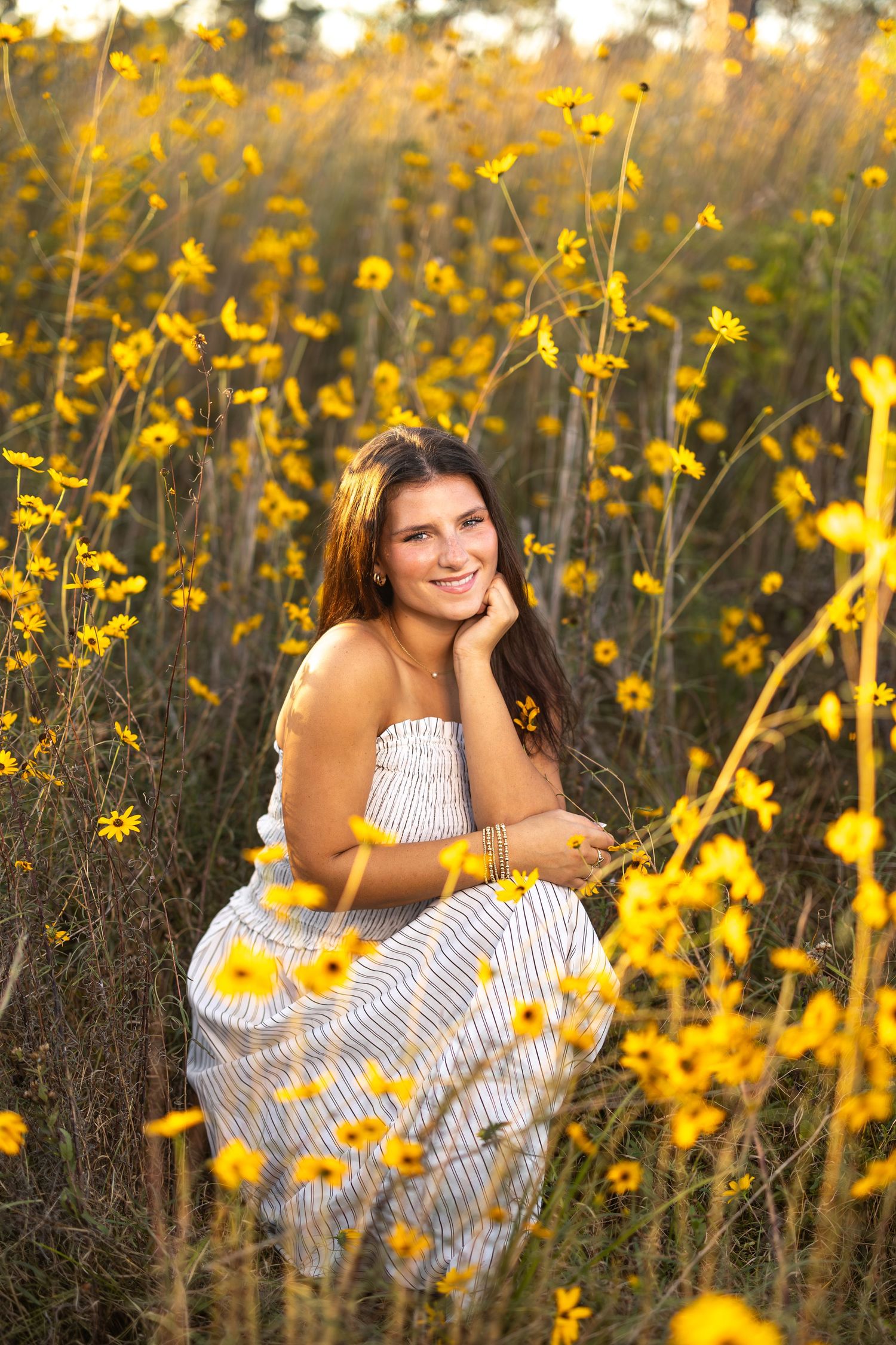Person in striped dress poses among blooming yellow wildflowers at golden hour.