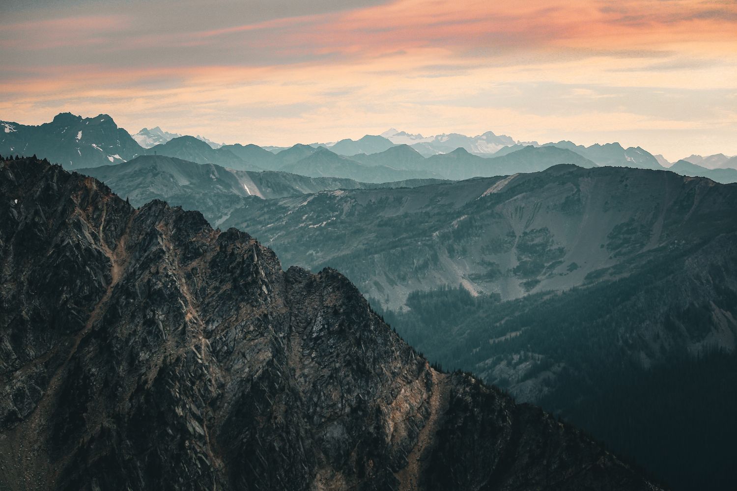 Panoramic view of rugged mountain peaks under a pink and orange sunset sky.