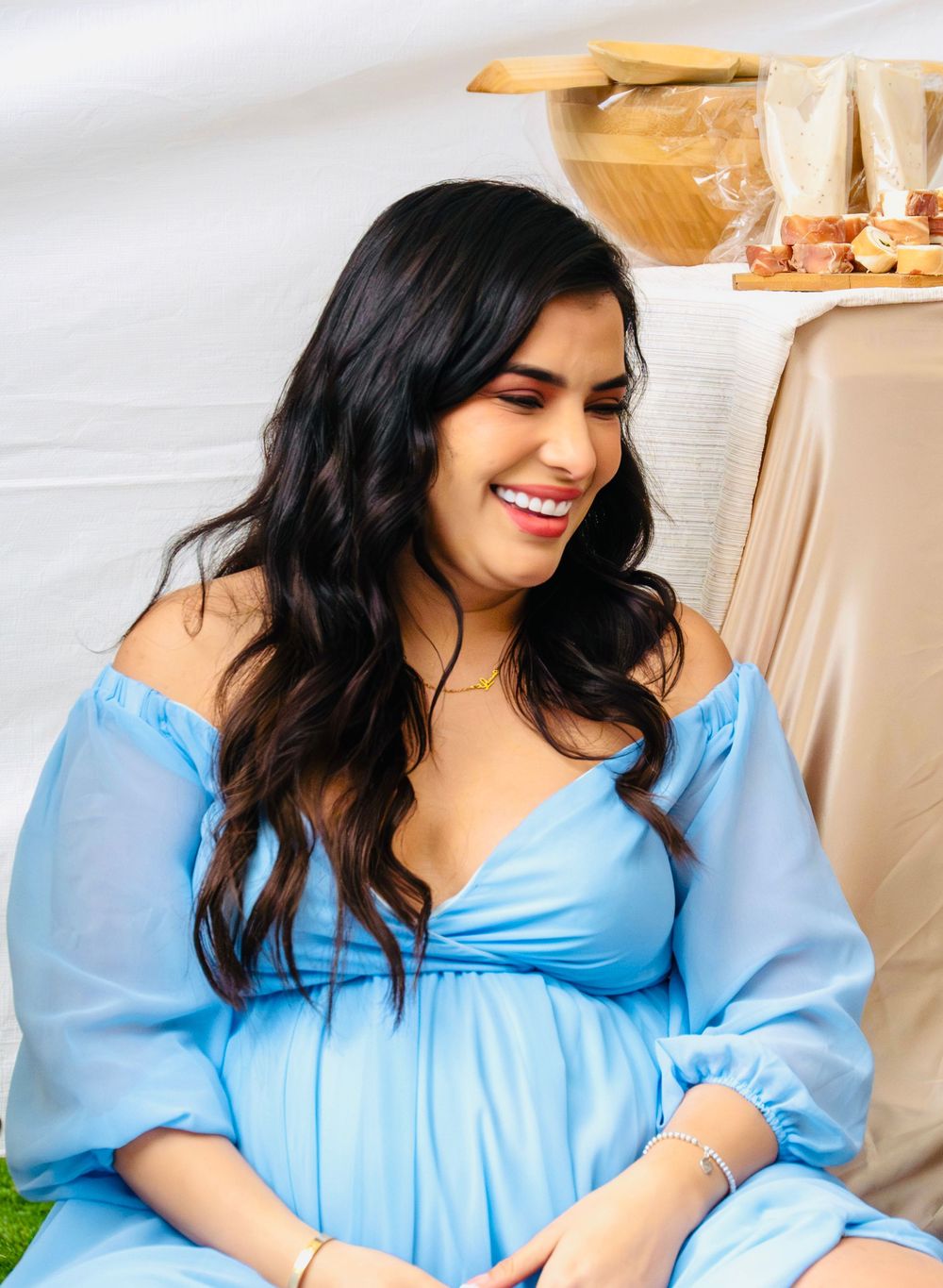 Beautiful pregnant woman in a blue off-shoulder dress smiling joyfully at her elegant outdoor baby shower.