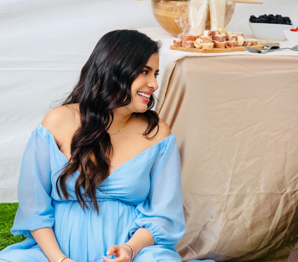 Happy pregnant woman in a flowing blue dress smiling at an elegant outdoor baby shower event.