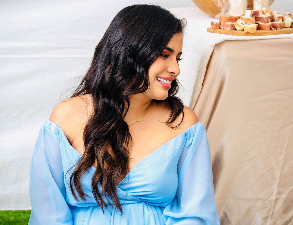 Glowing pregnant woman in a blue off-shoulder maternity dress smiling at an outdoor baby shower.