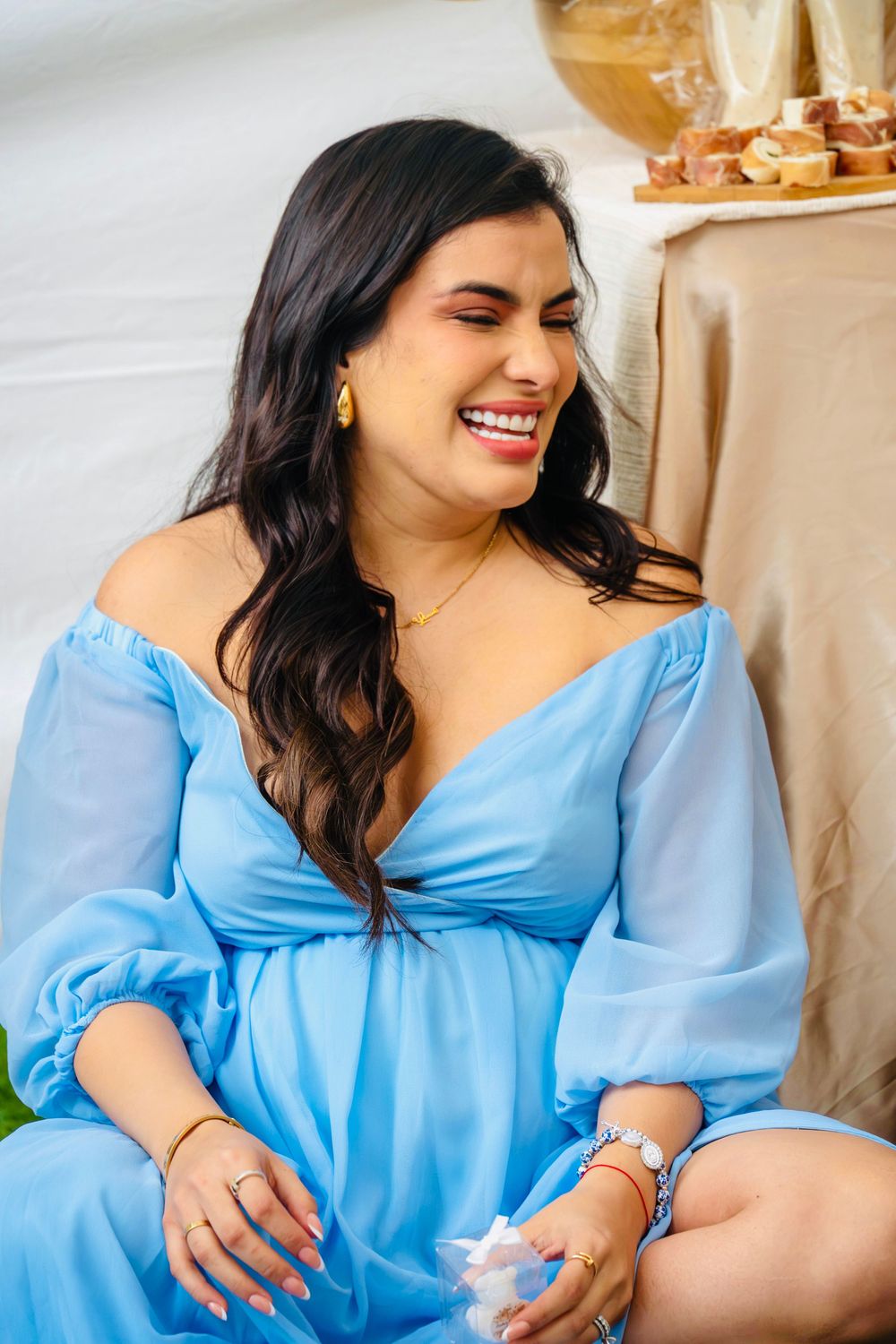 Radiant pregnant woman in blue off-shoulder dress laughing joyfully at her baby shower celebration.