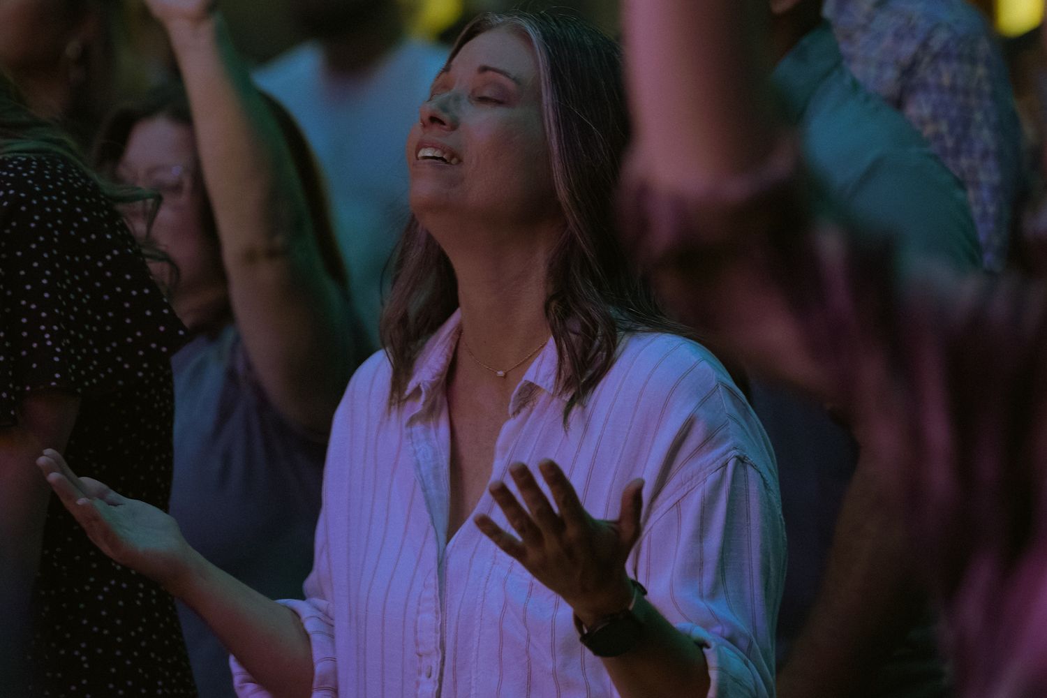 Concert audience with raised hands worshipping during evening service.