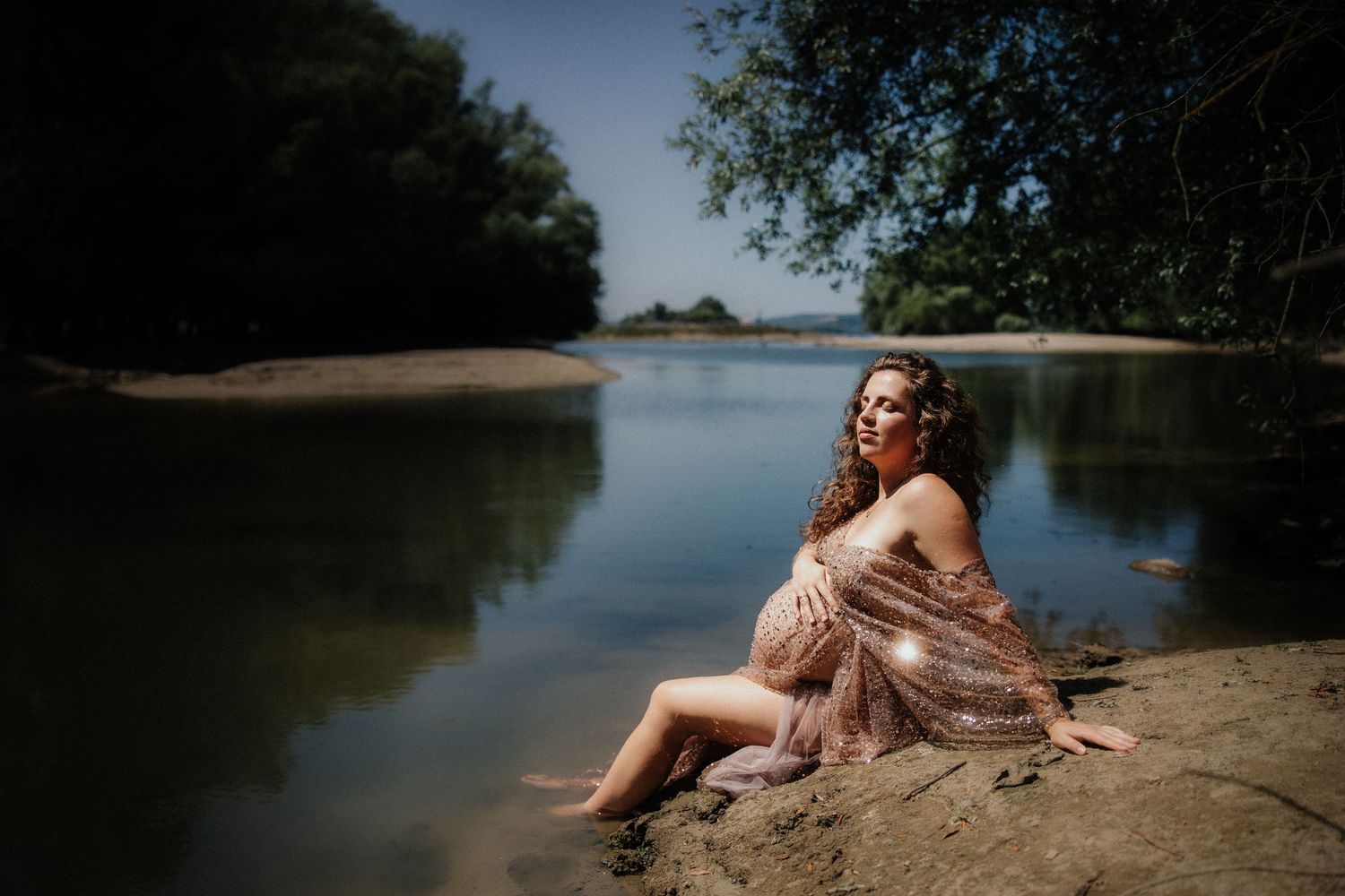 Woman in red swimsuit lounges on sandy beach near calm lake waters on sunny summer day.