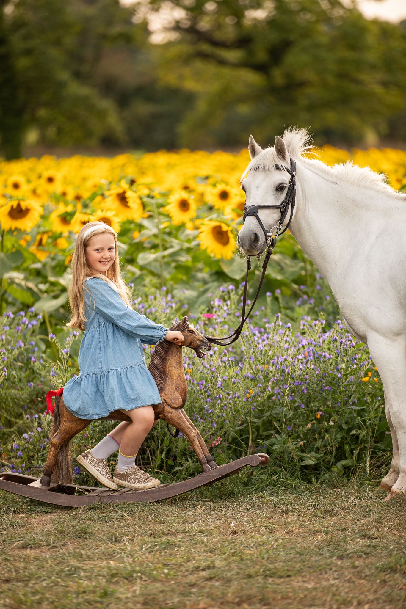 Young girl in denim overalls embraces a palomino horse in a sun-dappled forest setting.