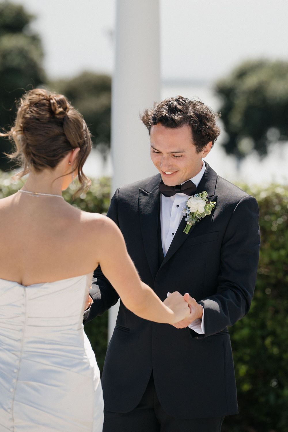 A couple shares a joyful moment during their wedding ceremony, with the bride in white and groom in black tuxedo.