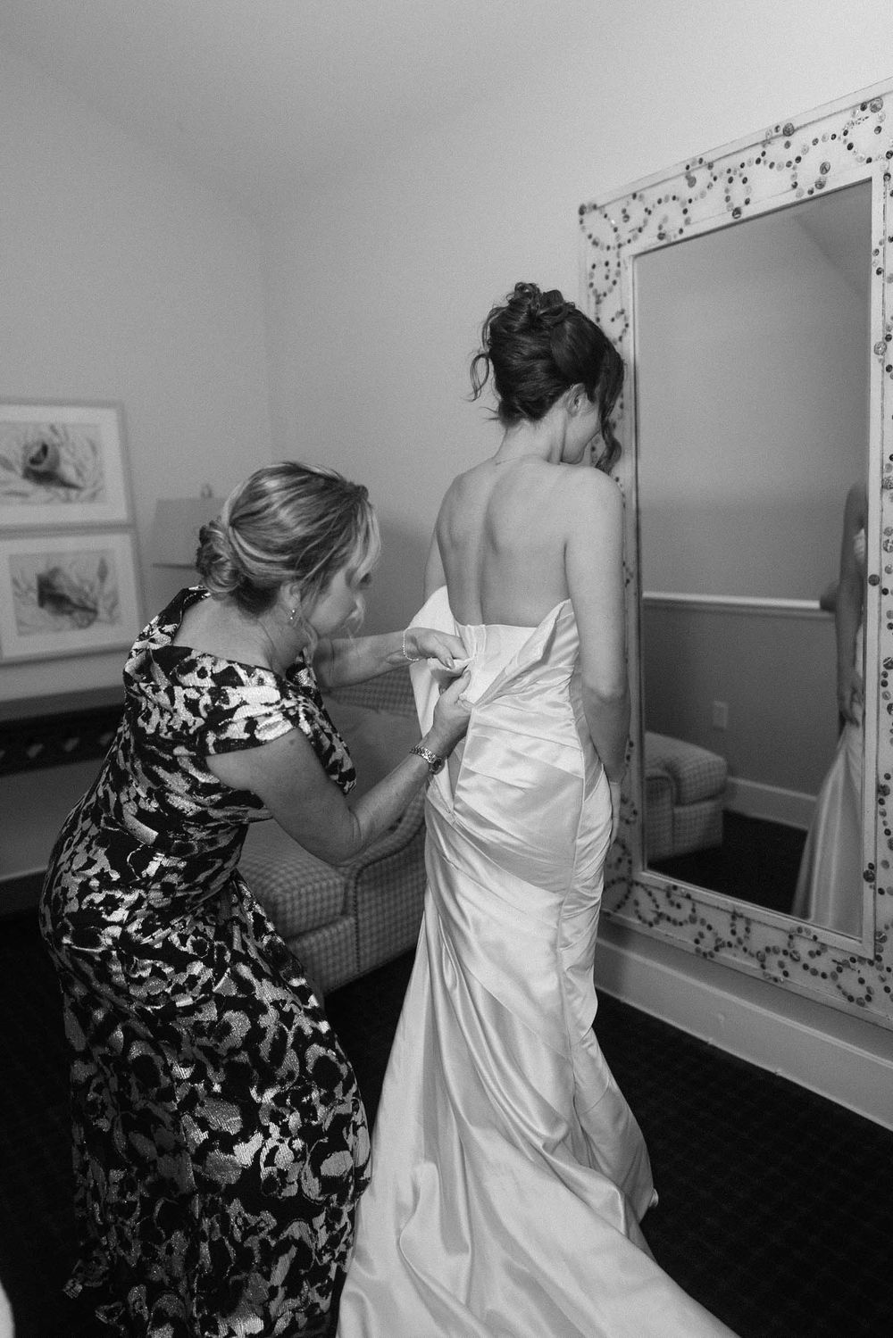 Black and white photo series showing a wedding dress being adjusted and fitted in a dressing room.