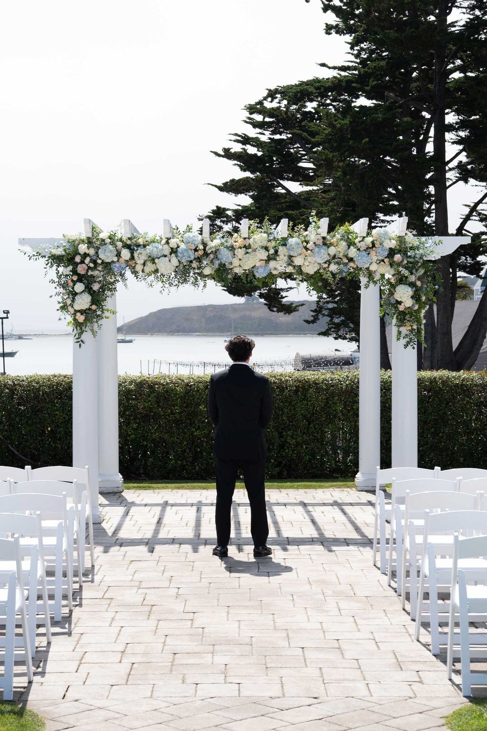 White wedding ceremony setup with chairs and floral arch overlooking a scenic mountain landscape.