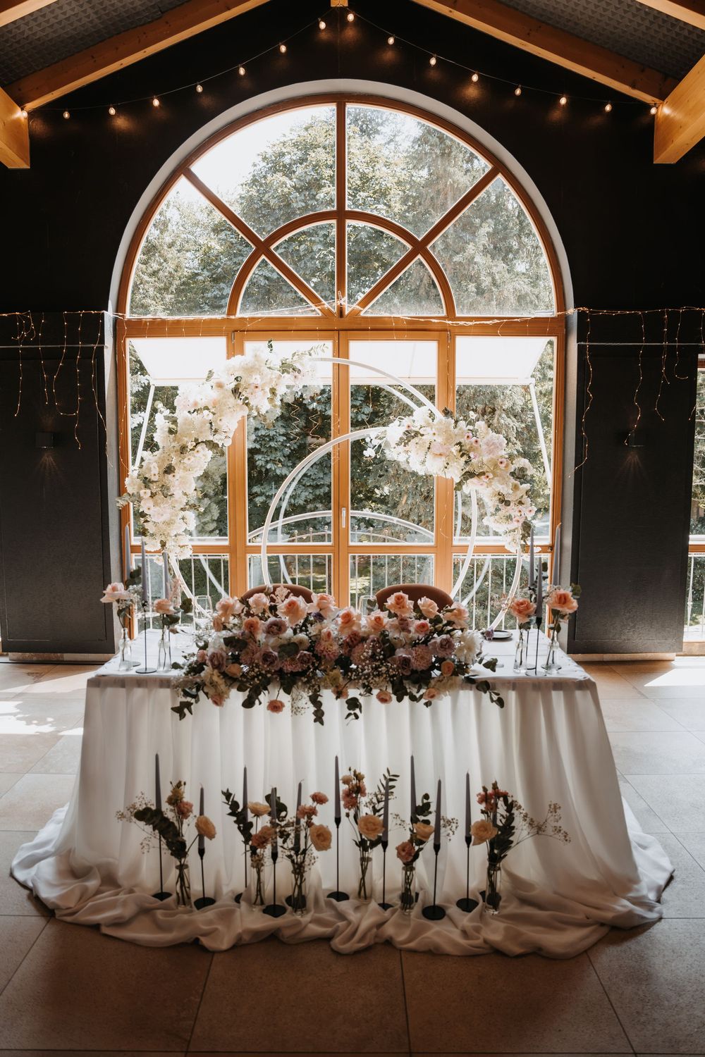 Elegant wedding sweetheart table with peach and white floral arrangements before an arched window.