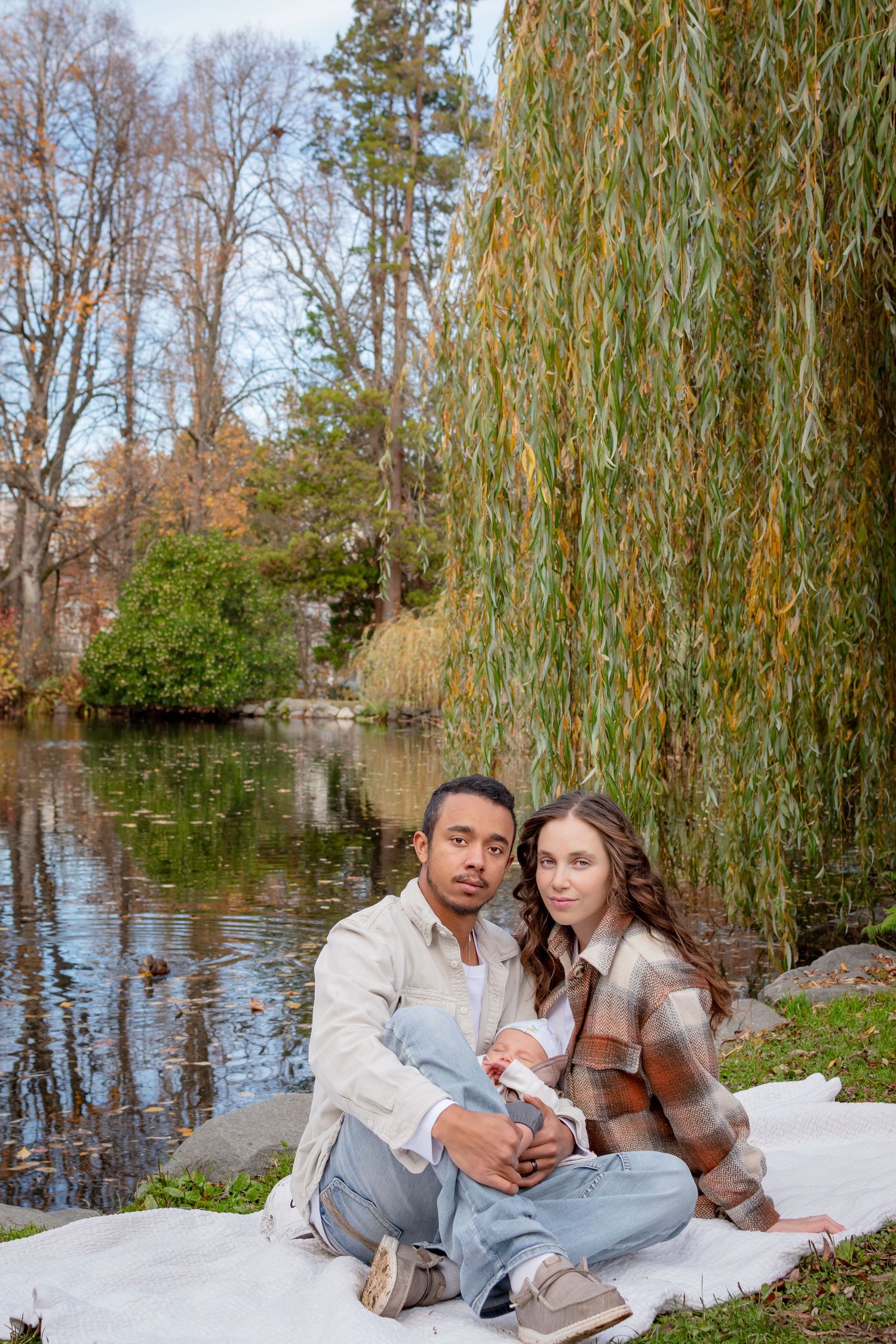 Family sitting by the pond under willow trees during a fall photo session at Wright Park in Tacoma.
