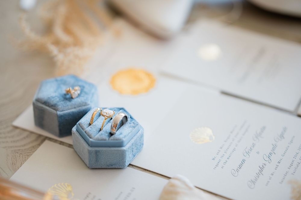 Light blue ring boxes and elegant wedding invitations arranged on a white surface with soft candlelight.