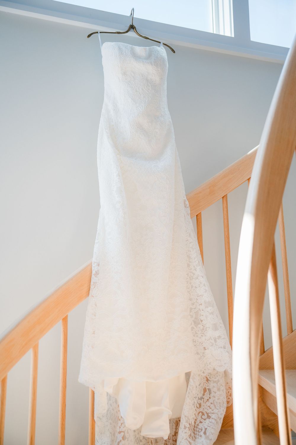 White lace wedding dress hanging gracefully against a light wall with wooden accents.