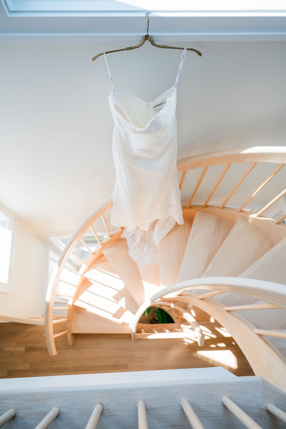 Ethereal wedding dress suspended in natural light with chairs creating artistic shadows below.