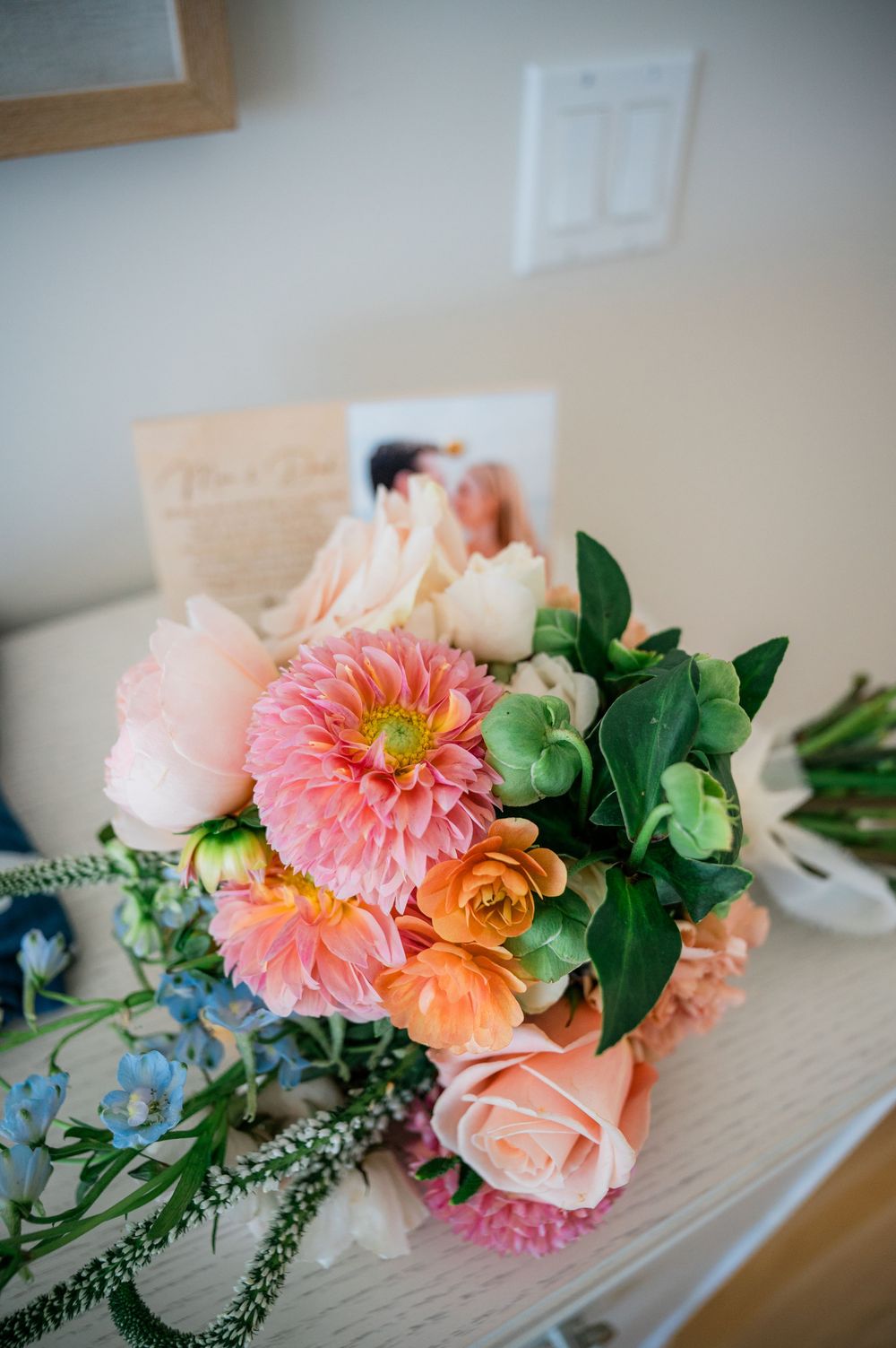 Fresh floral arrangement with pink dahlias, roses, and green foliage on a light surface.