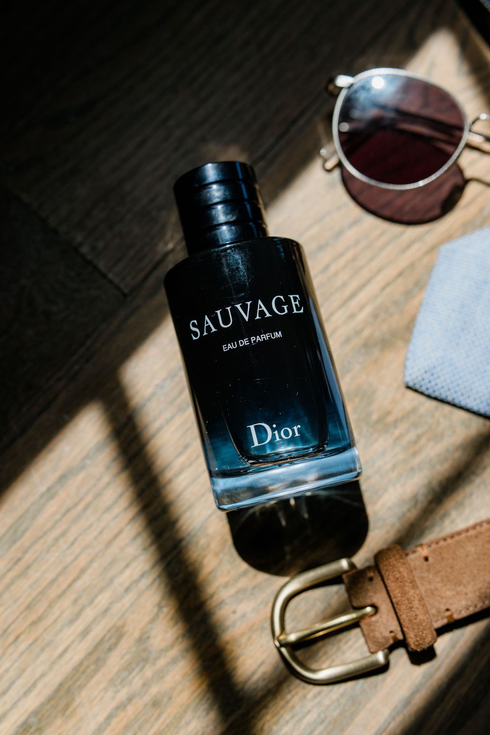 Dior Sauvage perfume bottle casting dramatic shadows on wooden surface.
