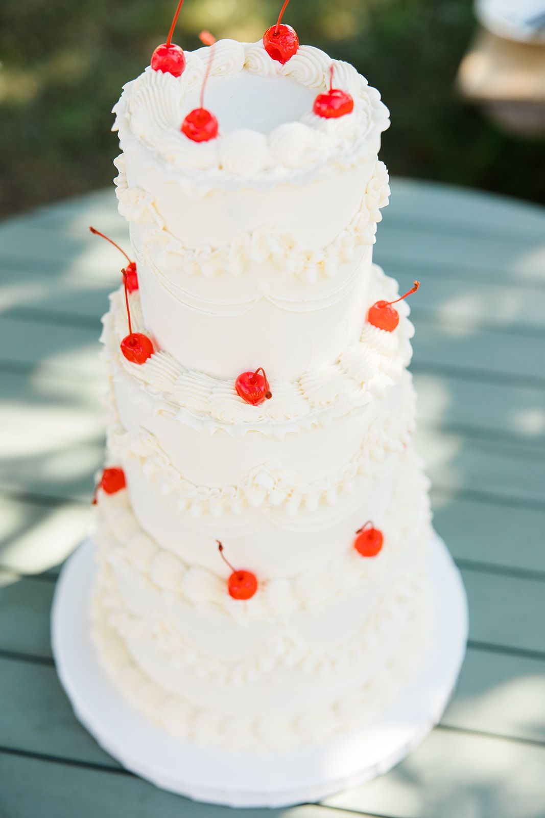 A white three-tiered wedding cake decorated with whipped cream and topped with bright red maraschino cherries.