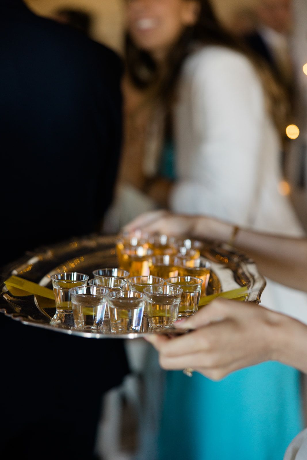 Server carrying tray of small shot glasses filled with drinks at an event reception.
