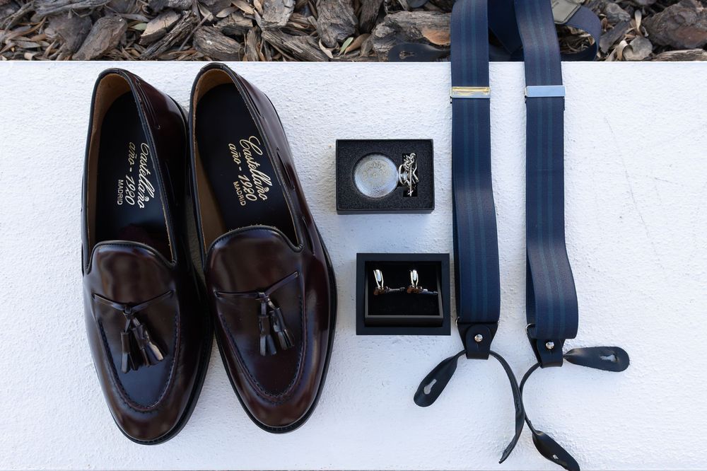 A collection of brown leather dress shoes and black belts arranged in a row on a white surface.