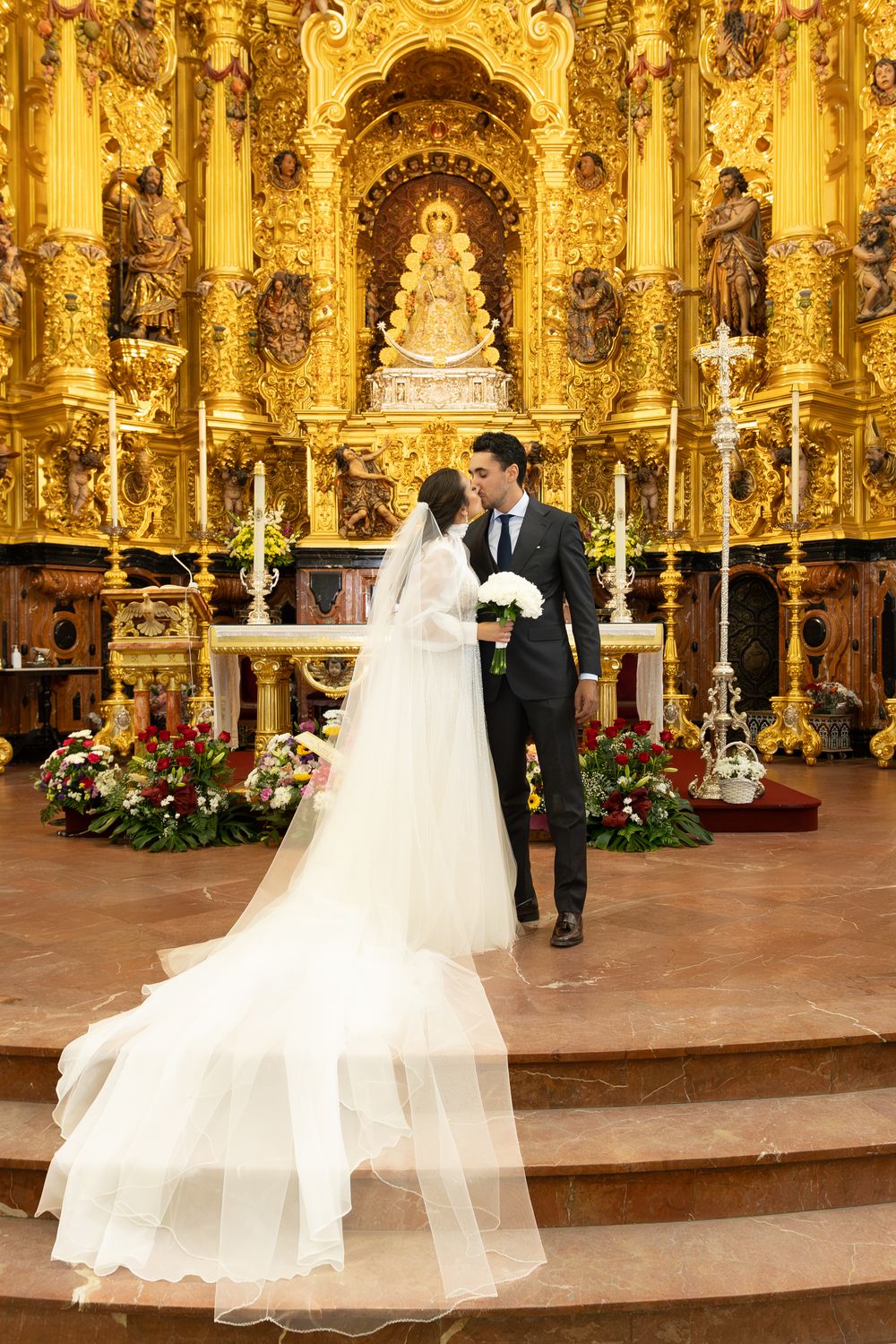 Wedding couple standing before magnificent gold baroque altar during ceremony.
