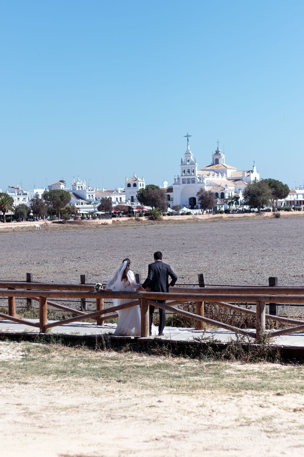 Wedding couple walking on wooden boardwalk with white church and buildings in background.