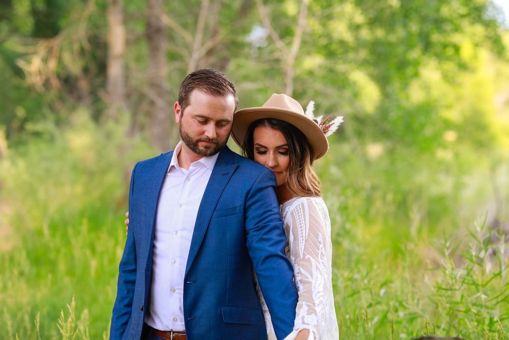 A couple in formal attire shares an intimate moment while walking through a lush green outdoor setting.
