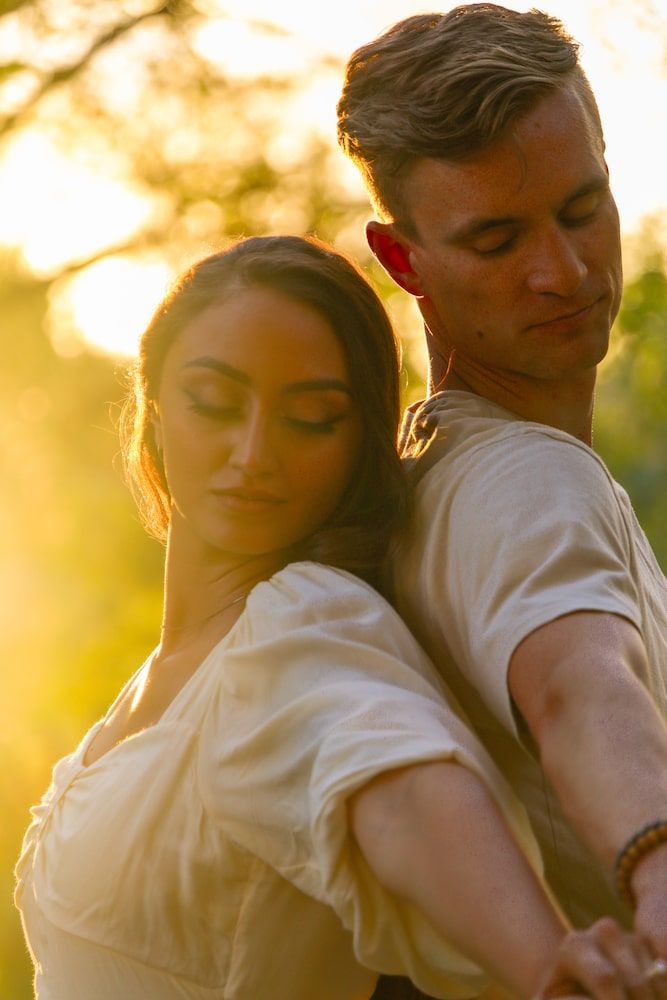 A romantic couple embraces in a golden sunset glow while wearing white and looking peaceful and content.