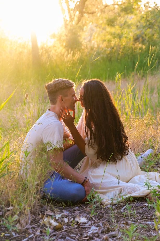 A couple lies together in a sunlit meadow surrounded by tall grass during golden hour.