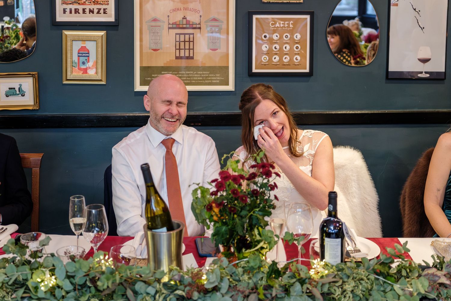 Wedding reception guests seated at a long table decorated with lush greenery and floral centerpieces.