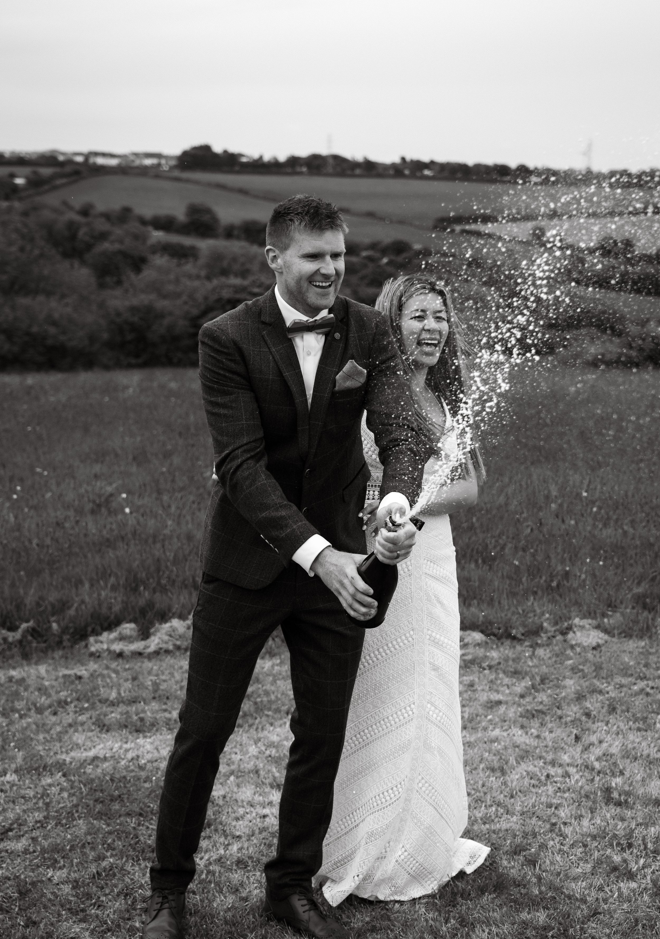 Black and white photo of a couple celebrating with confetti in an outdoor field.