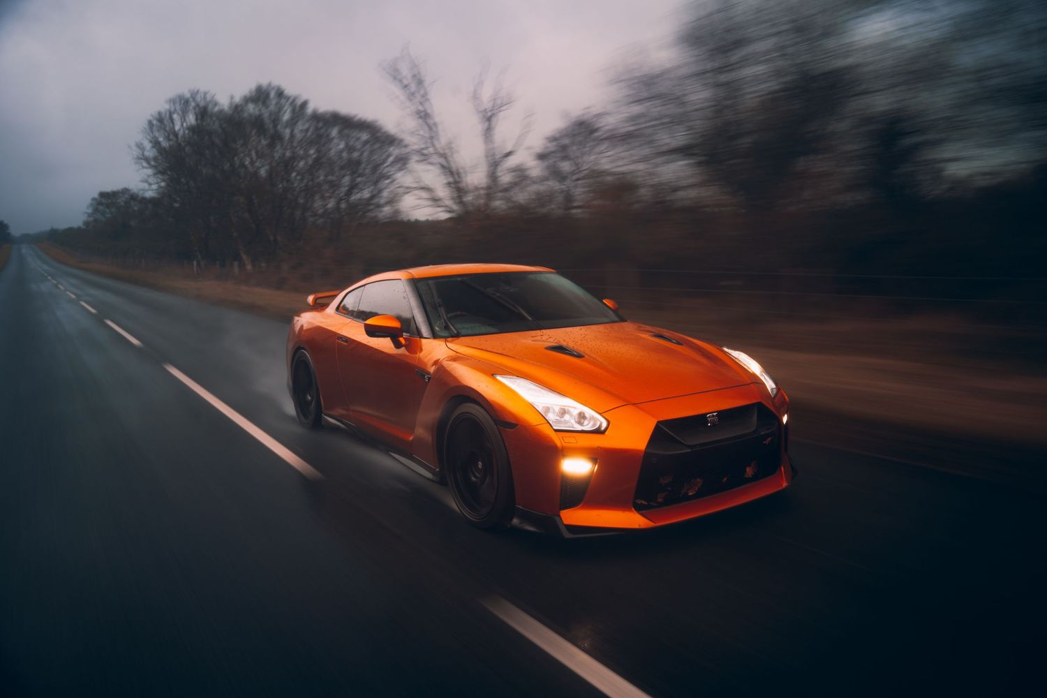 Orange sports car photographed with dynamic motion blur on forest road.