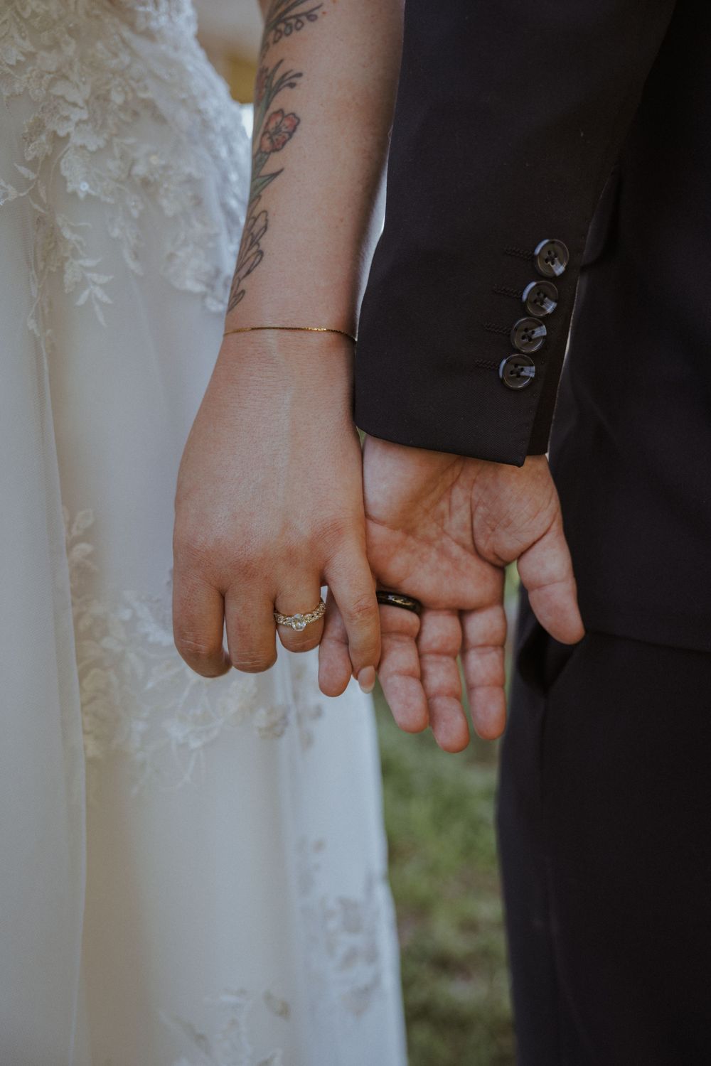 Close-up of newlyweds' hands showing wedding rings and tattoo details.