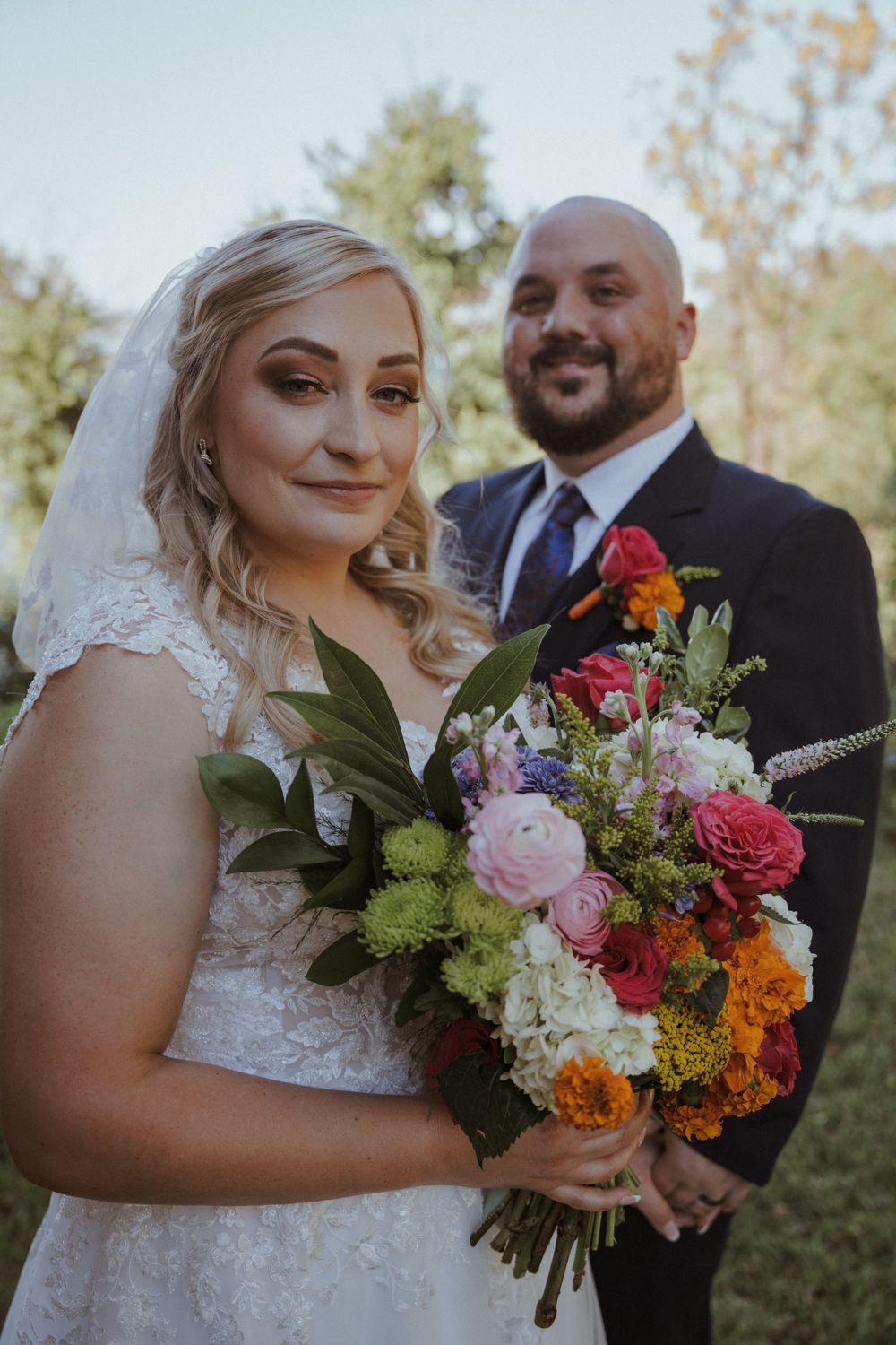 Outdoor wedding portraits with vibrant mixed flower bouquet against natural scenery.