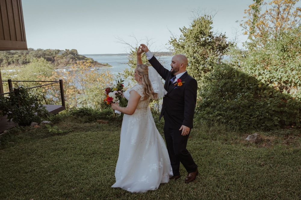 Newlyweds dance together on a hillside with ocean views in the background.