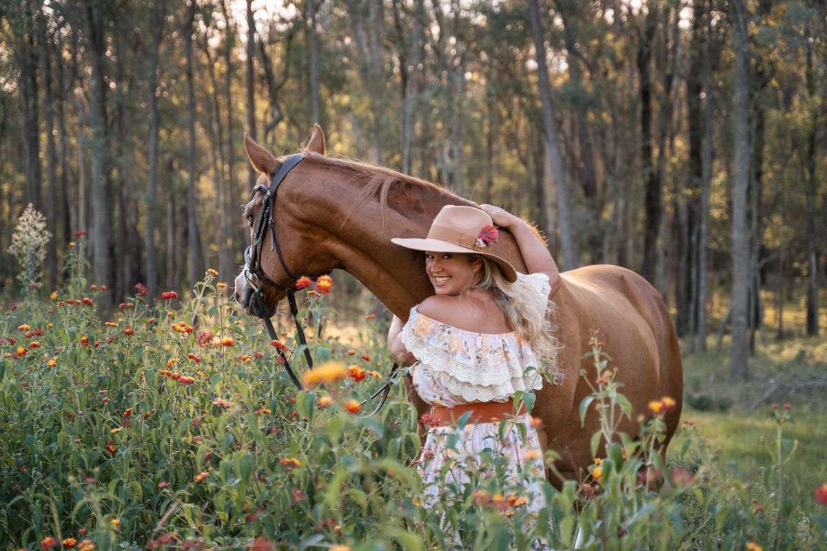 A chestnut horse grazes in a sunlit forest clearing surrounded by tall trees and wildflowers with a girl during a horse photoshoot in sydney