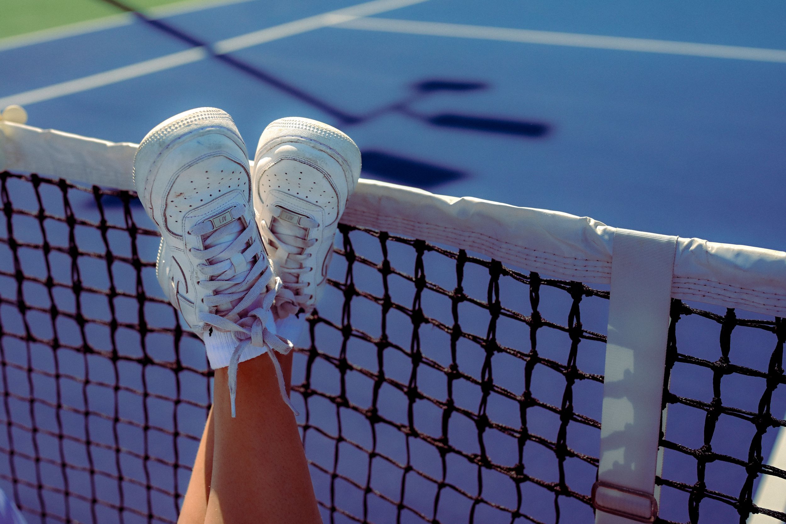 Tennis player wearing white serves the ball on a blue court during a competitive match.