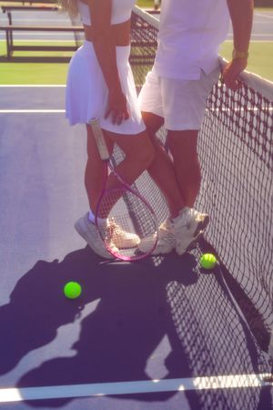Close-up of tennis ball and feet near the net during a match on a sunny court.
