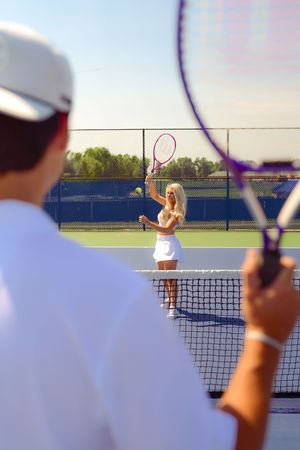 Tennis players practicing serves and returns across the net on an outdoor court at sunset.
